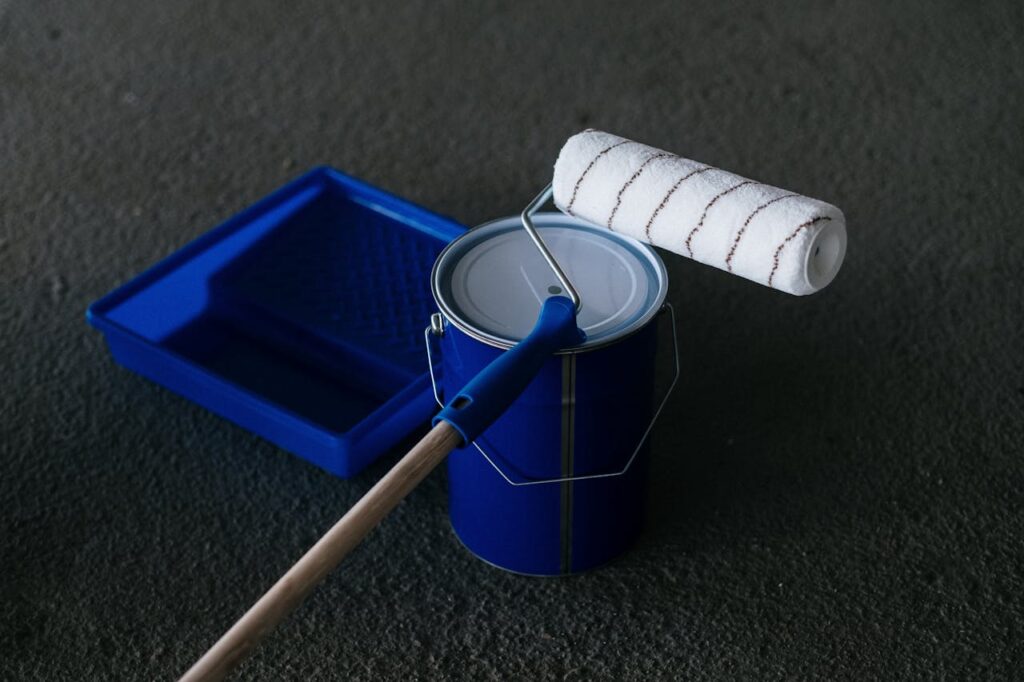 Close-up of a paint can, roller, and tray on a textured floor, perfect for DIY projects.